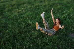 A young woman is playing in the park with us in the grass and falls to the ground smiling happily in the sunlight. Resting in nature, harmony with the body photo