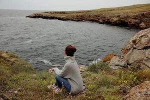 pretty woman in a gray sweater stands on a rocky shore nature Relaxation concept photo