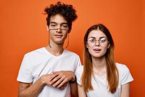 curly guy and a girl in white t-shirts are standing next to each other on an orange background photo