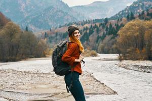 woman in sweater with a backpack rest in the mountains near the river in autumn in nature and tall trees model photo