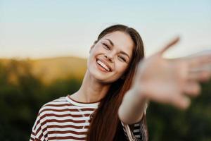 Woman smiling while looking at the camera and pulling her hands to the camera close-up in nature with a view of the mountains. Happy travel lifestyle follow me photo