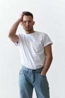 Portrait shot of handsome serious tanned man guy in basic t-shirt holds hand on head looks at camera posing on white background. Fashion Style New Collection Offer. Copy space for ad. Model snap photo