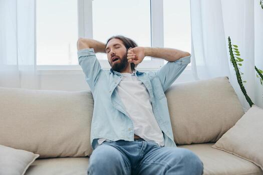 A man sits on the couch yawning and stretching after a nap, lack of sleep and fatigue from work and improper daily routine. photo