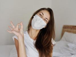 woman sitting on bed wearing medical mask positive gesture hand emotion photo