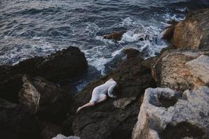 beautiful young woman in a secluded spot on a wild rocky coast in a white dress unaltered photo