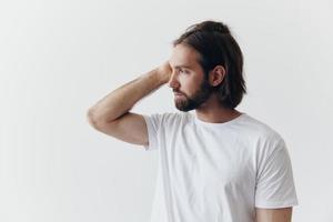 Portrait of a man with a black thick beard and long hair in a white T-shirt on a white isolated background emotion of sadness and longing photo