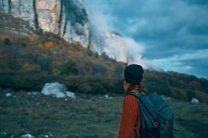 a traveler with a backpack and in a red sweater shows the mountains with her hand and the blue sky clouds photo