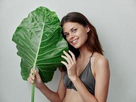 cheerful woman in a swimsuit green leaf in hands exotic light background photo