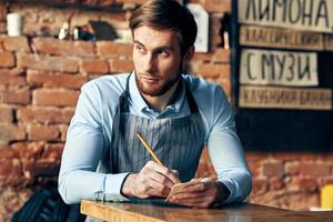 a man in an apron sits at a table accepting an order a cafe waiter photo