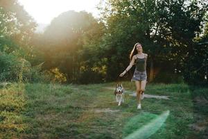 un mujer carreras con un perro en el bosque durante un noche caminar en el bosque a puesta de sol en otoño. estilo de vida Deportes formación con tu amado perro foto