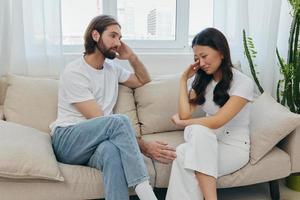 A man and a woman of different races sit on the couch in a room at home and talk about their problems to each other. A stress-free lifestyle of family quarrels with psychological support photo