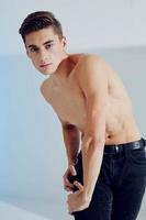 Handsome young man in black pants on a light background and a naked torso photo