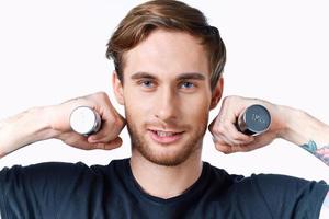 a sporty man in a black t-shirt holds dumbbells near his face on a light background and a black t-shirt photo