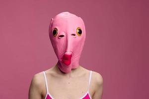 Conceptual art photo of a sexy woman in a fish mask for Halloween on a pink background