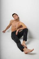 Handsome man in black trousers sits on the floor naked torso studio attractiveness photo