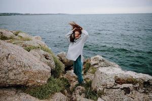 bonito mujer en un gris suéter soportes en un rocoso apuntalar naturaleza inalterado foto