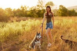 A woman laughs and plays with a dog in nature in a field smiling hugging a husky dog photo