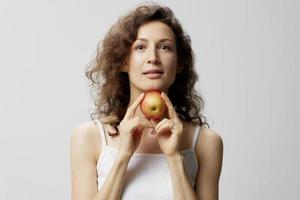 Smiling lovely cute curly beautiful woman in basic white t-shirt pulls apple enjoy healthy food posing isolated on over white background. Natural Eco-friendly products concept. Copy space photo