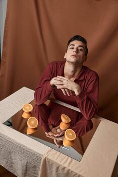 man at table with mirror and oranges looking up cropped view photo