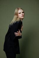 Art fashion photo shoot. Professional blonde model holds herself hugs with both hands half-turned looks at the camera posing on a green background in the studio