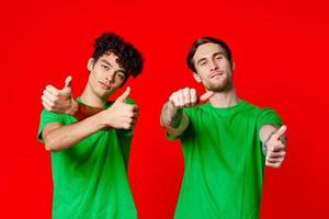 Cheerful friends in green t-shirts gesturing with hands emotions red background photo