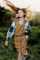 Woman walking on the grass in nature smiling in farm clothes with beautiful hair flying in the wind happy in the rays of summer sunset light photo