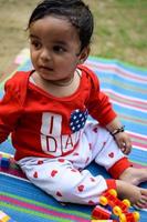 Cute little Indian infant sitting enjoying outdoor shoot at society park in Delhi, Cute baby boy sitting on colourful mat with grass around, Baby boy outdoor shoot photo