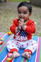 linda pequeño indio infantil sentado disfrutando al aire libre disparar a sociedad parque en Delhi, linda bebé chico sentado en vistoso estera con césped alrededor, bebé chico al aire libre disparar foto