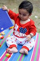 Cute little Indian infant sitting enjoying outdoor shoot at society park in Delhi, Cute baby boy sitting on colourful mat with grass around, Baby boy outdoor shoot photo