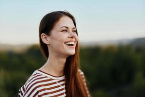 Close-up portrait of a young woman with a beautiful smile with teeth in a striped t-shirt against the background of trees photo