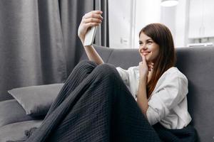 woman sitting on sofa and taking pictures of herself on the phone gray plaid curtains interior photo