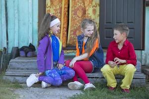 gracioso pequeño niños muchachas con brillante maquillaje vestido en el estilo de el noventa y un chico en un rojo camisa son sentado en el pueblo foto