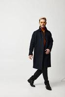 a man in a dark coat and trousers walks to the side on a light background trend of the season model photo