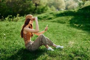 Lanza libre mujer trabajando en su teléfono en contra un verde verano paisaje, el estilo de vida de un blogger foto