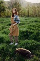 un granjero mujer en su trabajo ropa, tartán camisa y delantal, soportes en el campo en el verde césped y sonrisas en el ajuste Dom después un difícil días trabajo foto