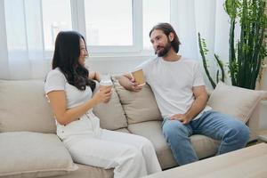 A man and a woman sitting at home on the couch in white stylish t-shirts and chatting merrily smiling and laughing at home. Male and female friendship photo