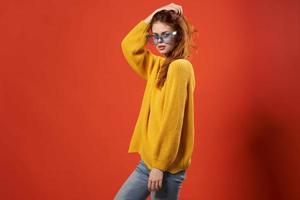 woman in a yellow sweater blue glasses studio fashionable hairstyle red background photo