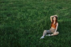 un niña en cómodo ropa se sentó en el césped después un caminar en el parque a meditar y descanso en el luz de sol foto