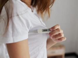 woman holding a thermometer under her arm behind a white t-shirt closeup photo