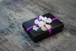 Black gift box with white flowers on wooden background photo