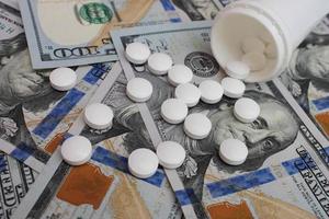 Pills spilling from container on the background of dollars photo