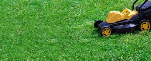 electric yellow and black lawn mower on green grass, copy space photo