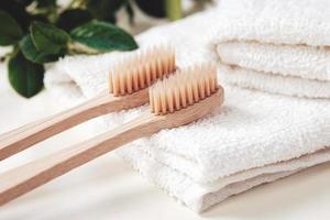 Bamboo toothbrushes, towels and green plant leaves in a bathroom photo