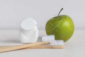 Bamboo toothbrushes, green apple and dental floss on white background photo