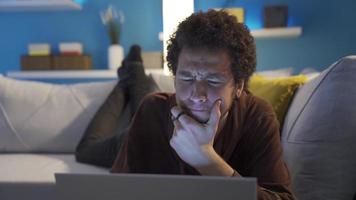 Young man looking at laptop at home thoughtful and confused. Teenager using laptop alone at home looking thoughtful and confused. video