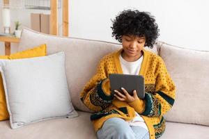 African american girl holding digital tablet touch screen typing scroll page at home. Woman with mobile tech device surfing internet using social media apps playing game. Study work shopping online. photo