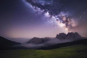 Milky Way over mountains in fog at night in summer. Landscape with foggy alpine mountain valley photo