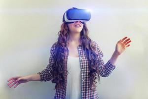 Smile young woman wearing using virtual reality VR glasses helmet headset on white background. Smartphone using with virtual reality goggles. Technology, simulation, hi-tech, videogame concept. photo