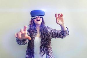 Smile young woman wearing using virtual reality VR glasses helmet headset on white background. Smartphone using with virtual reality goggles. Technology, simulation, hi-tech, videogame concept. photo
