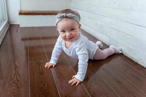 pequeña niña gateando de un año sentada en el suelo con luz brillante en la sala de estar cerca de la ventana sonriendo y riendo foto